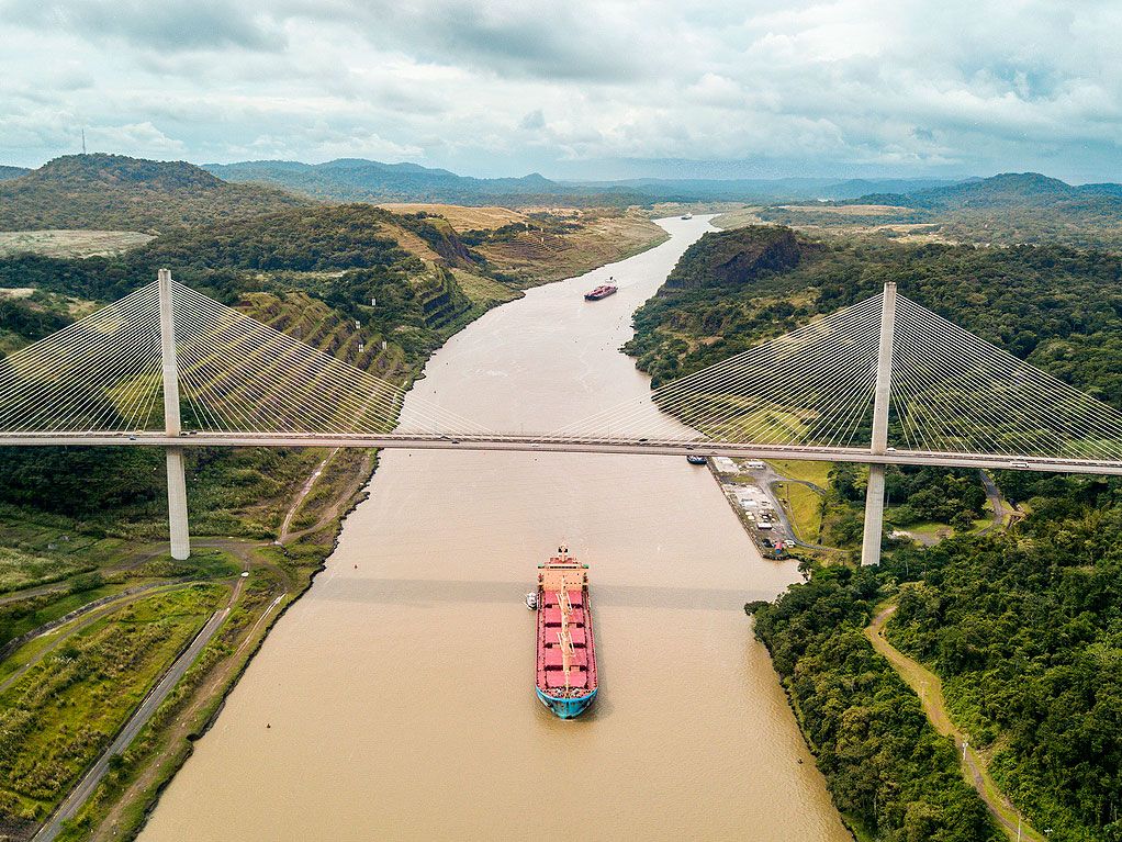 Aerial view of bridge spanning over Panama Canal and cargo ship passing underneath