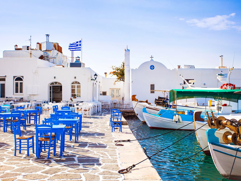 Blue and white patio chairs and tables alongside marina in Paros, Greece