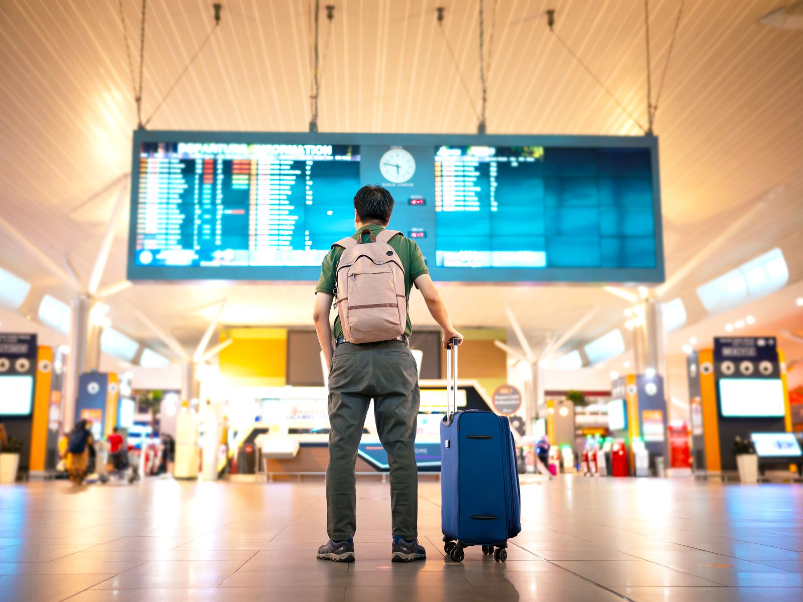 Traveler with backpack and suitcase looking at departures board in airport