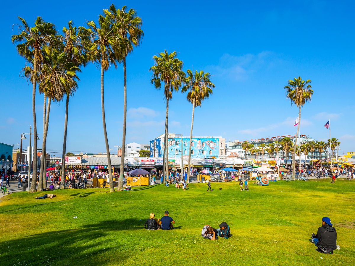 People sitting in park beside Venice Beach boardwalk in Los Angeles, California