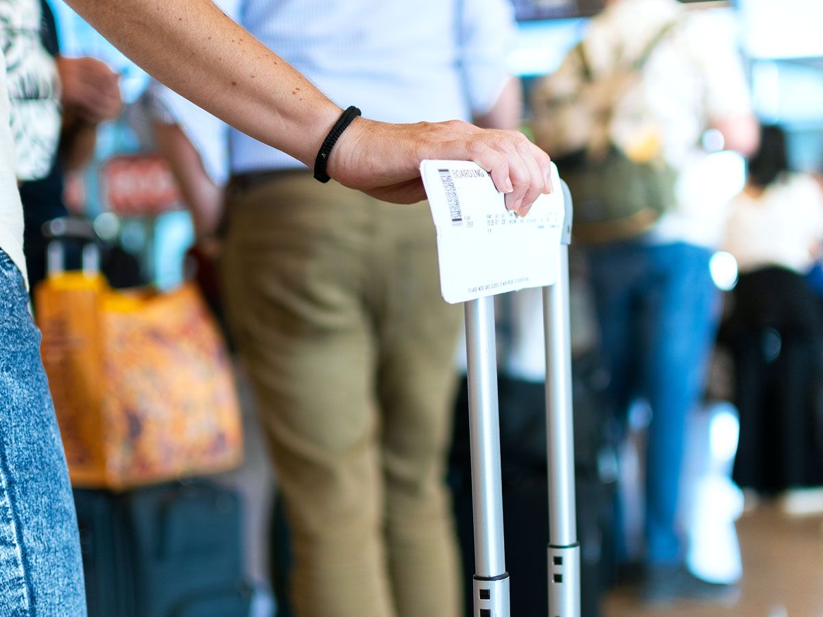 Traveler holding boarding pass and suitcase handle in airport line