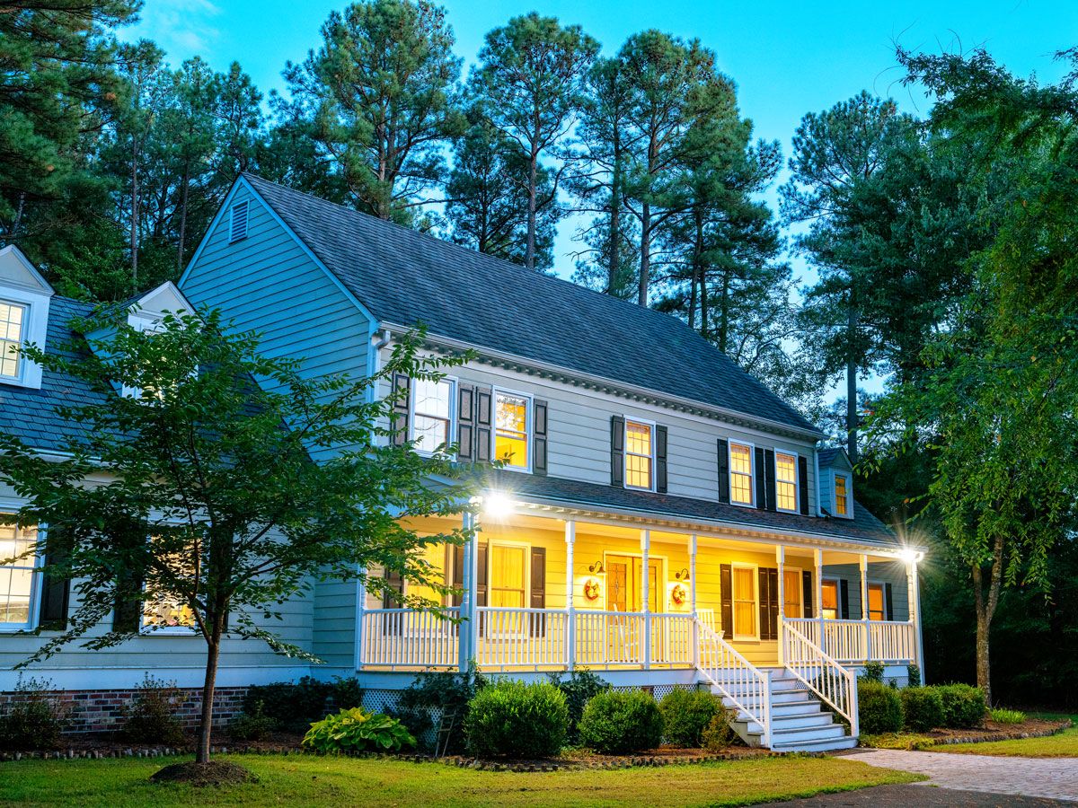 Colonial-style home with porch lights on during evening