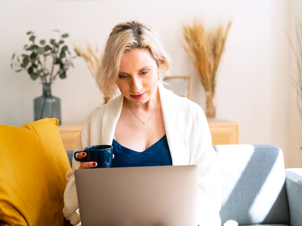 Woman sitting on couch with laptop and mug