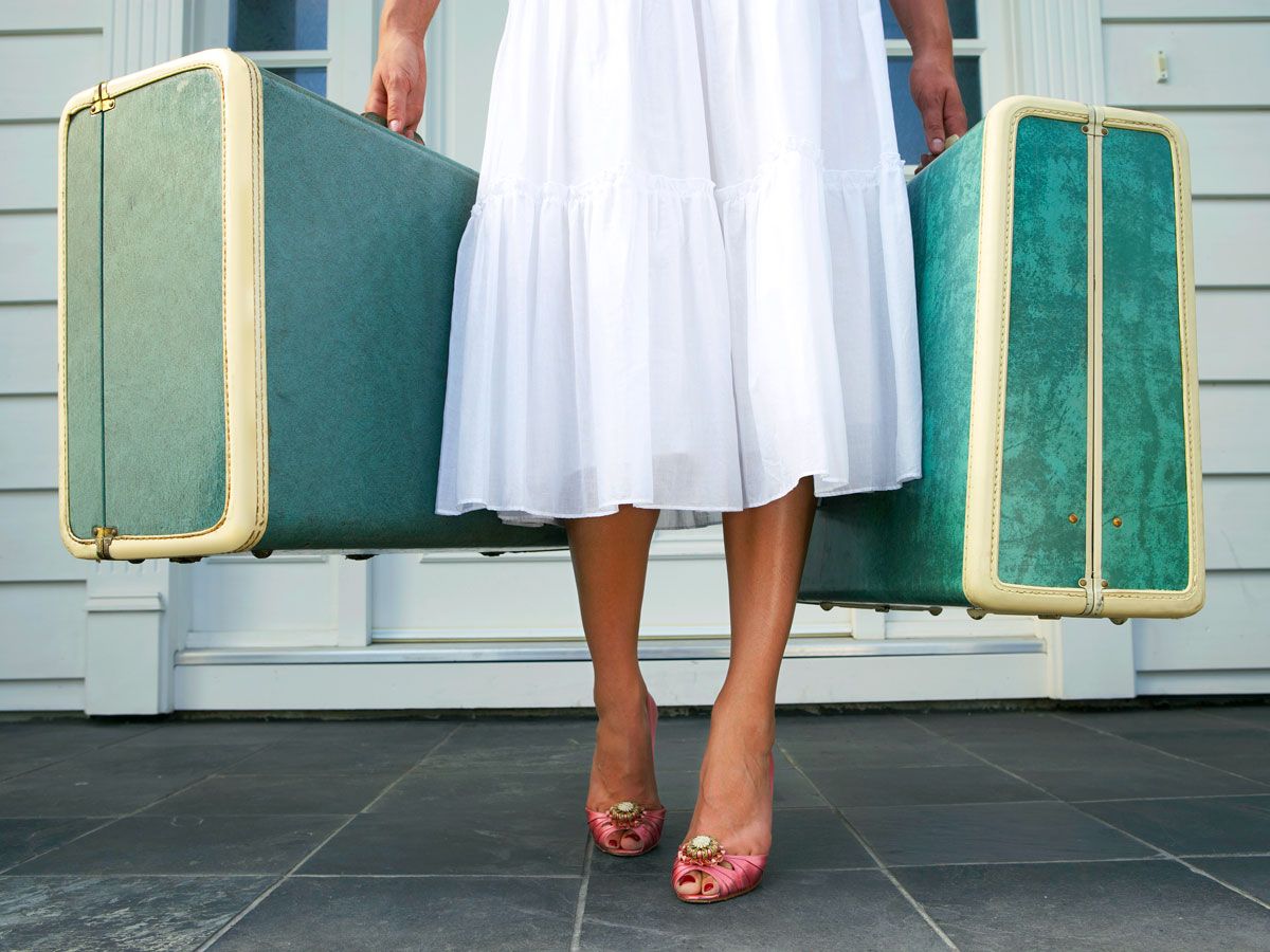 Woman carrying two suitcases wearing dress and heels