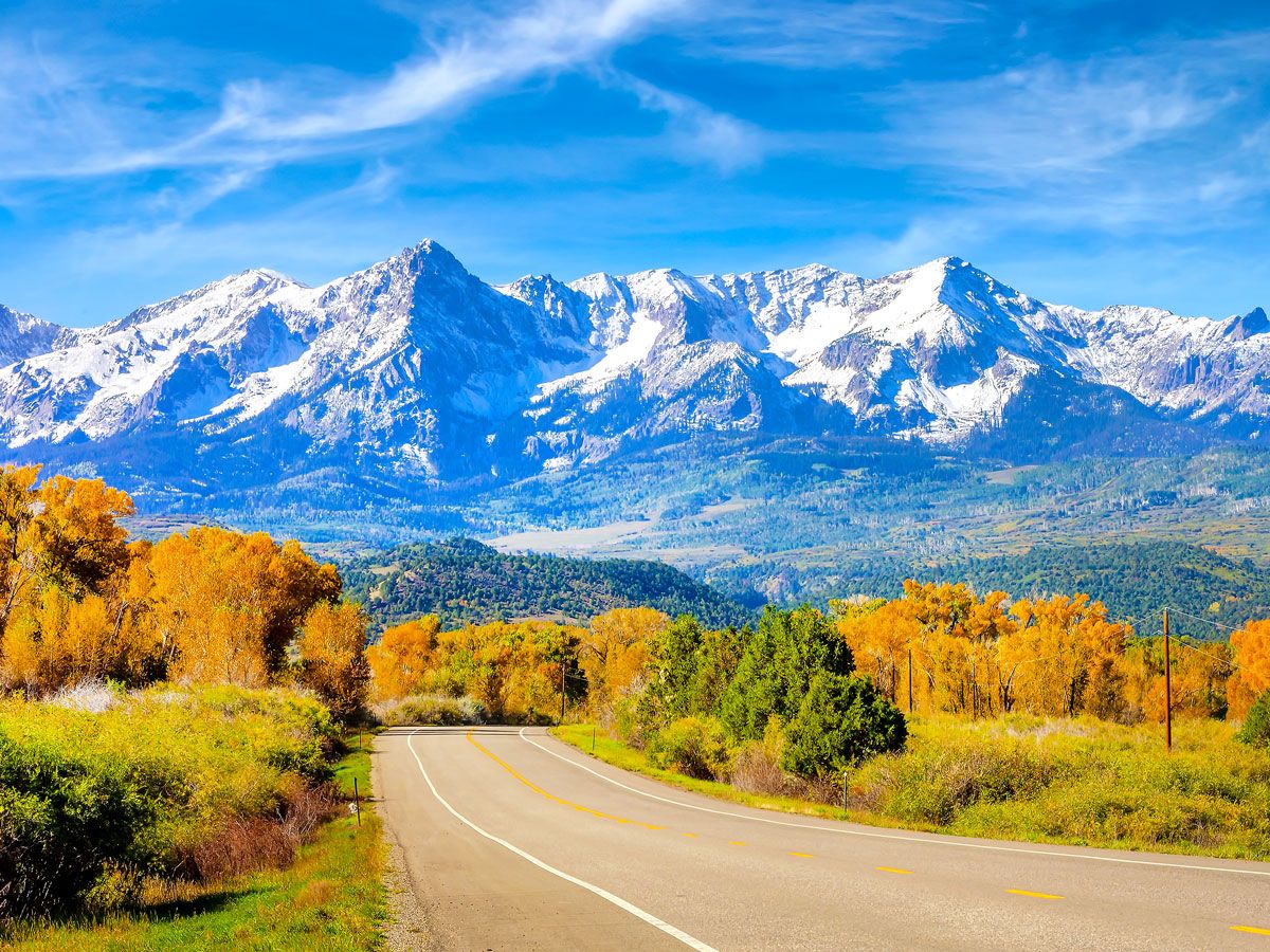 Empty Colorado highway with view of fall foliage and snowy peaks