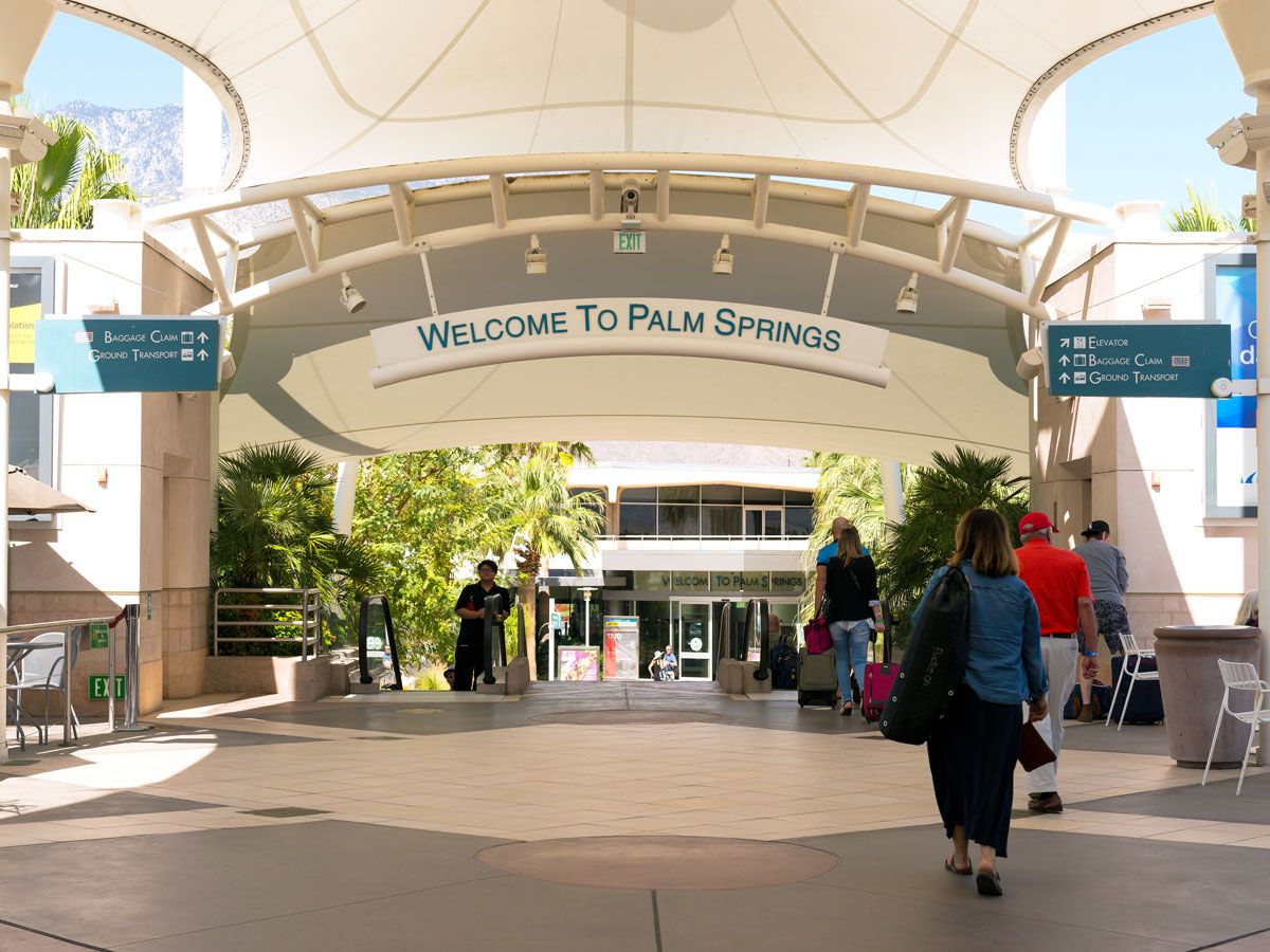 Passenger walking through outdoor area under "Welcome to Palm Springs" sign at Palm Springs International Airport