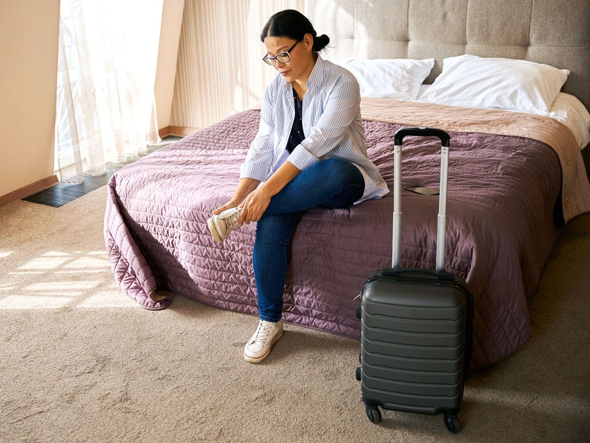 Traveler sitting on hotel room bed taking off shoe