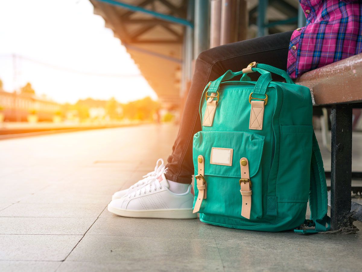 Traveler sitting on train platform bench with backpack on ground