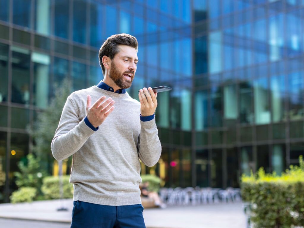 Man talking on speakerphone in front of building