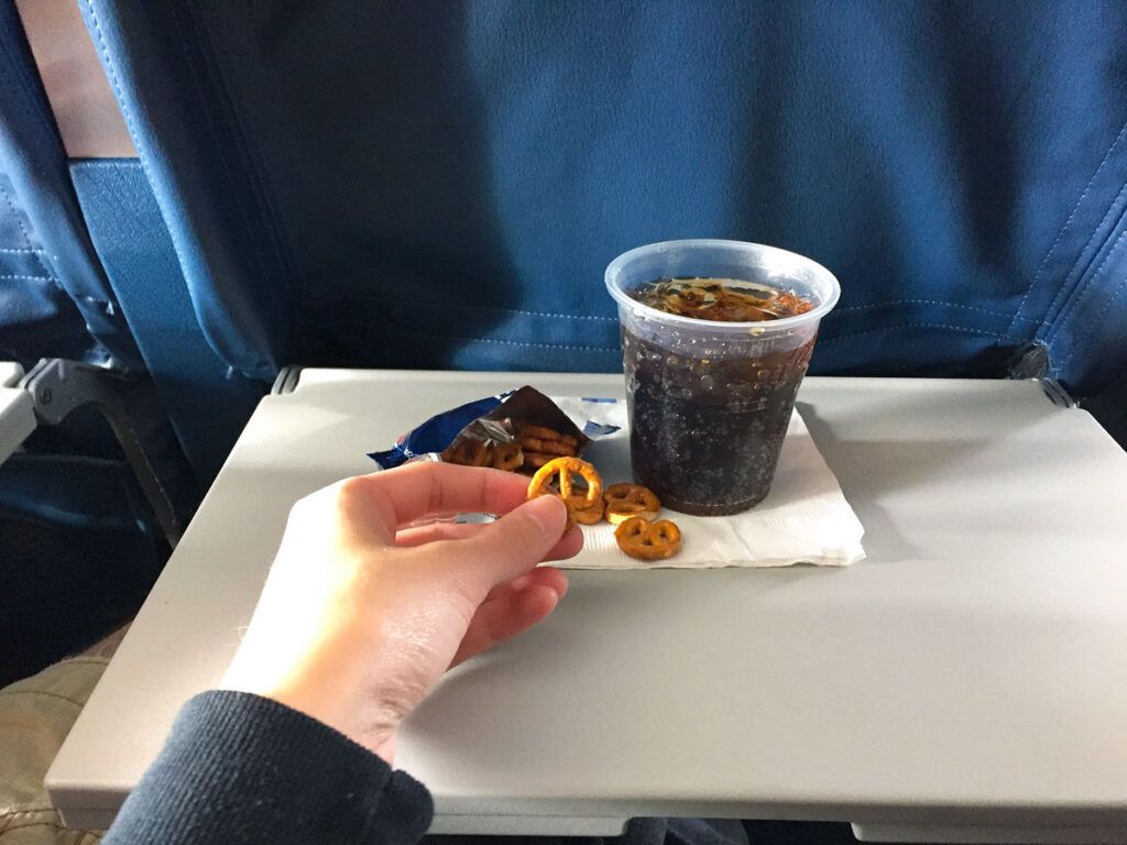 Passenger eating pretzels and drinking soda from tray table