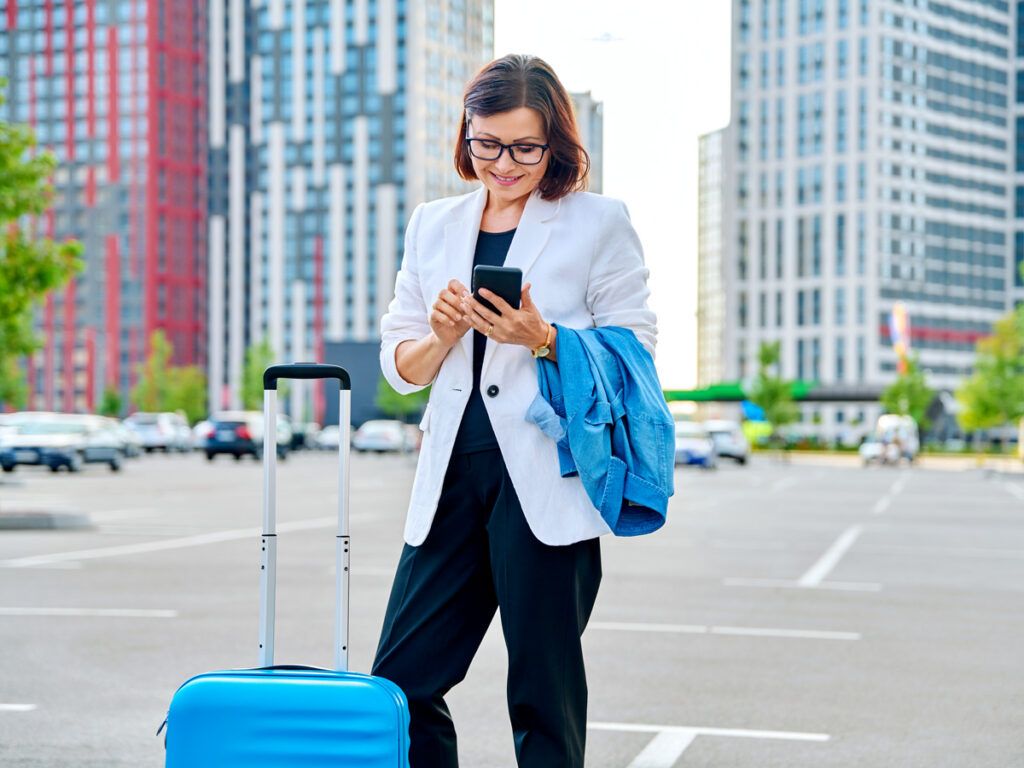 Traveler standing with suitcase and checking cellphone in parking lot