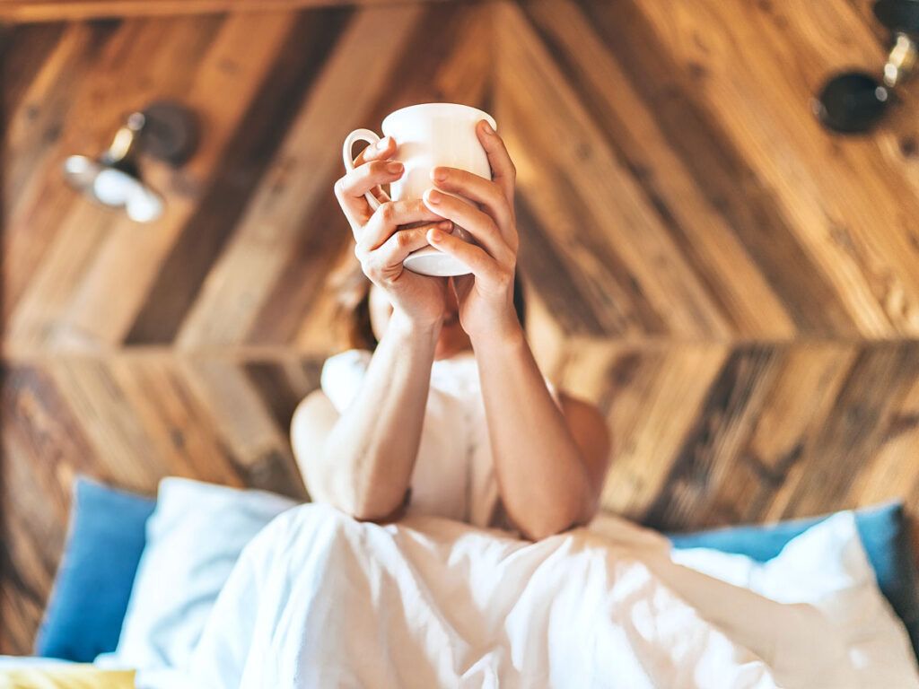 Person holding a cup of coffee in bed