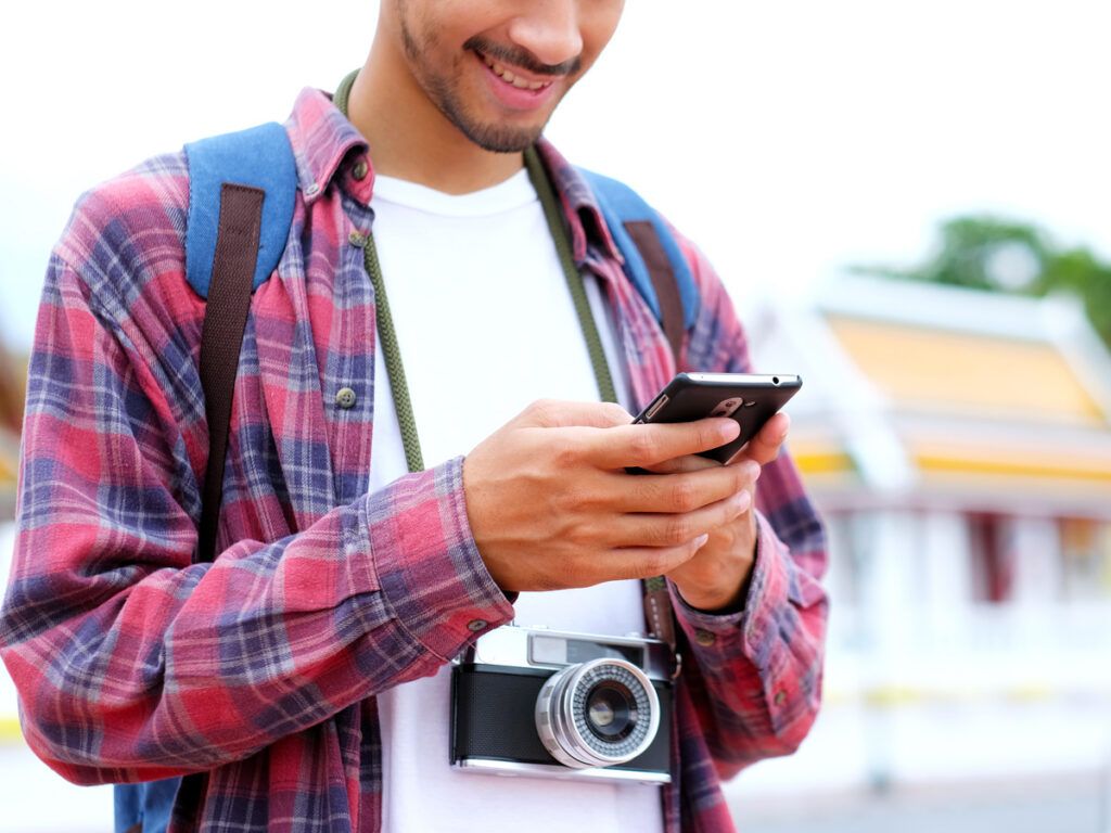 Tourist standing with camera and typing on cellphone