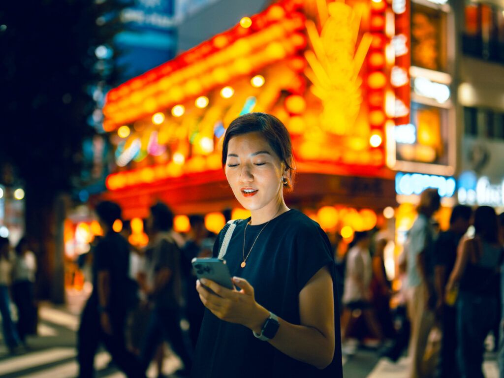 Woman standing on street corner at night looking at her phone