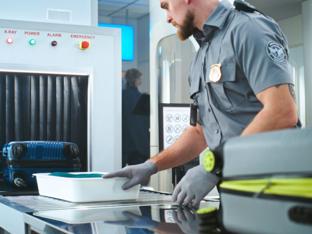 Security officer pushing bin through X-ray scanner
