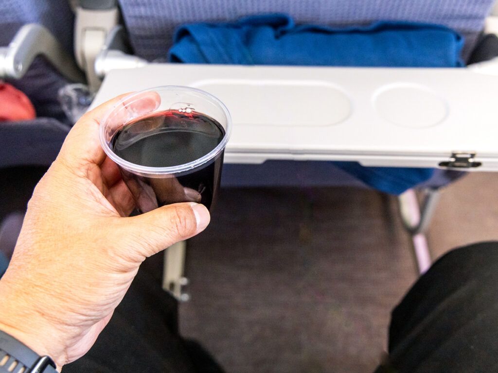 Passenger holding cup of red wine next to tray table