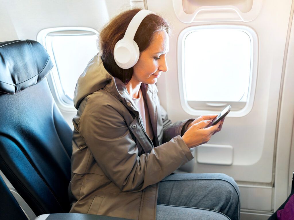 Airline passenger wearing headphones using cellphone