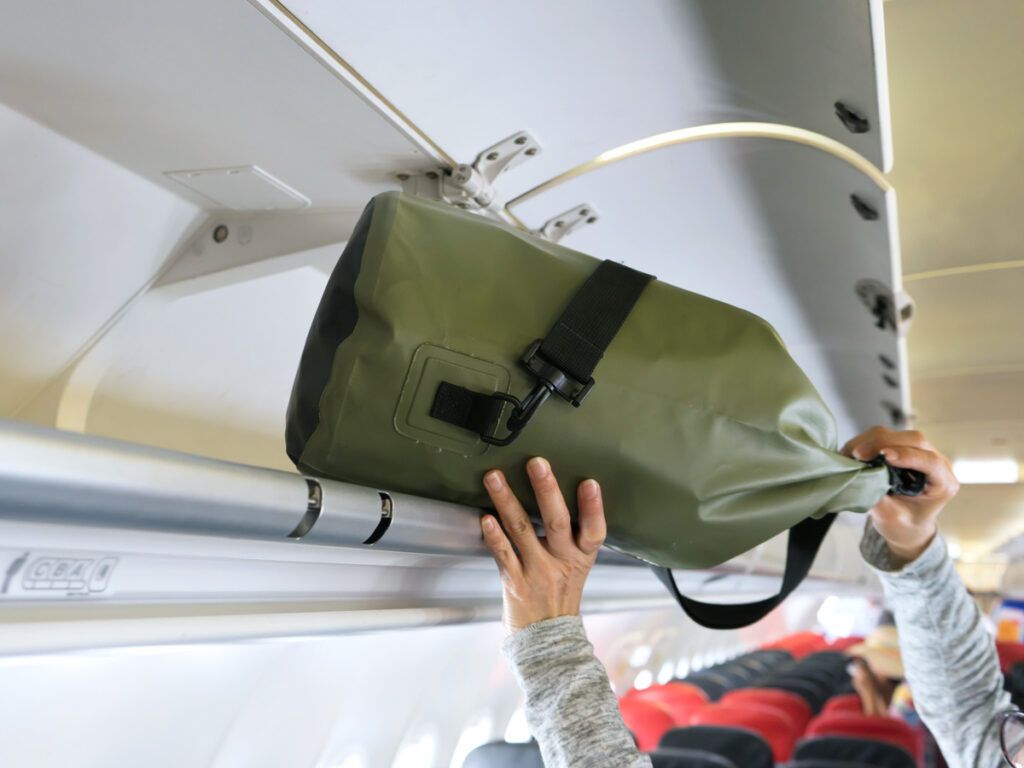Passenger stowing duffel bag in overhead bin