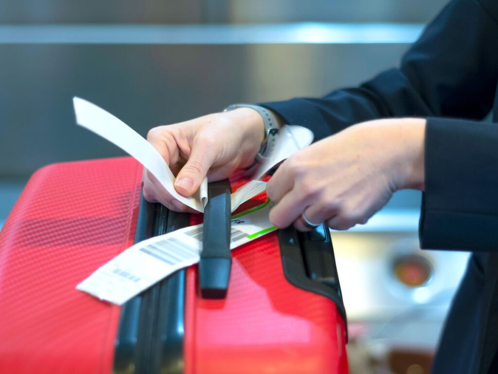 Check-in employee attaches a luggage tag to the suitcase of a passenger 