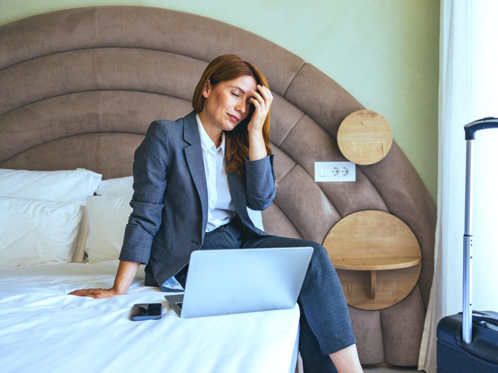 Woman sitting on hotel bed with laptop and phone