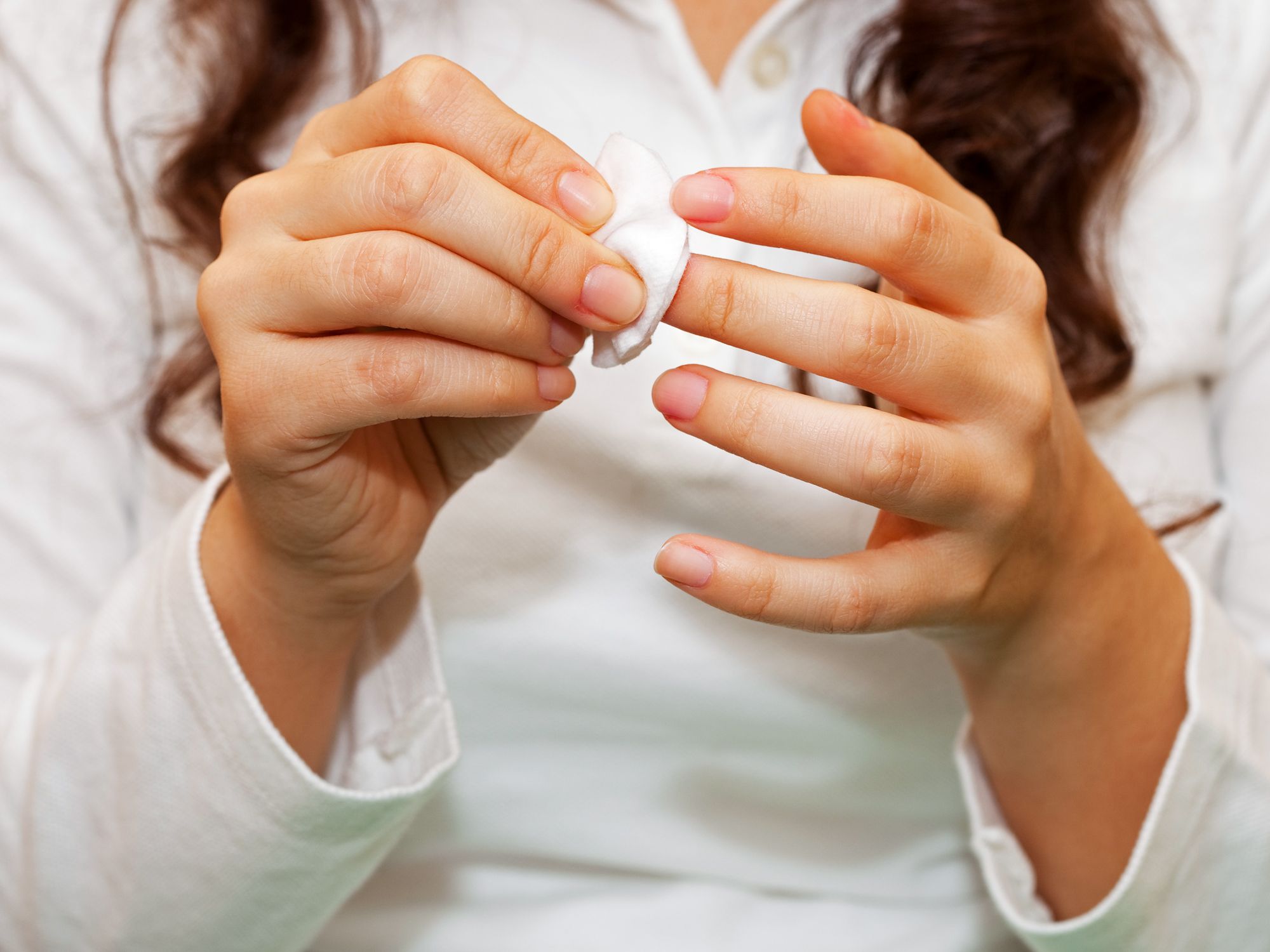 Person removing polish from fingernails with cotton pad