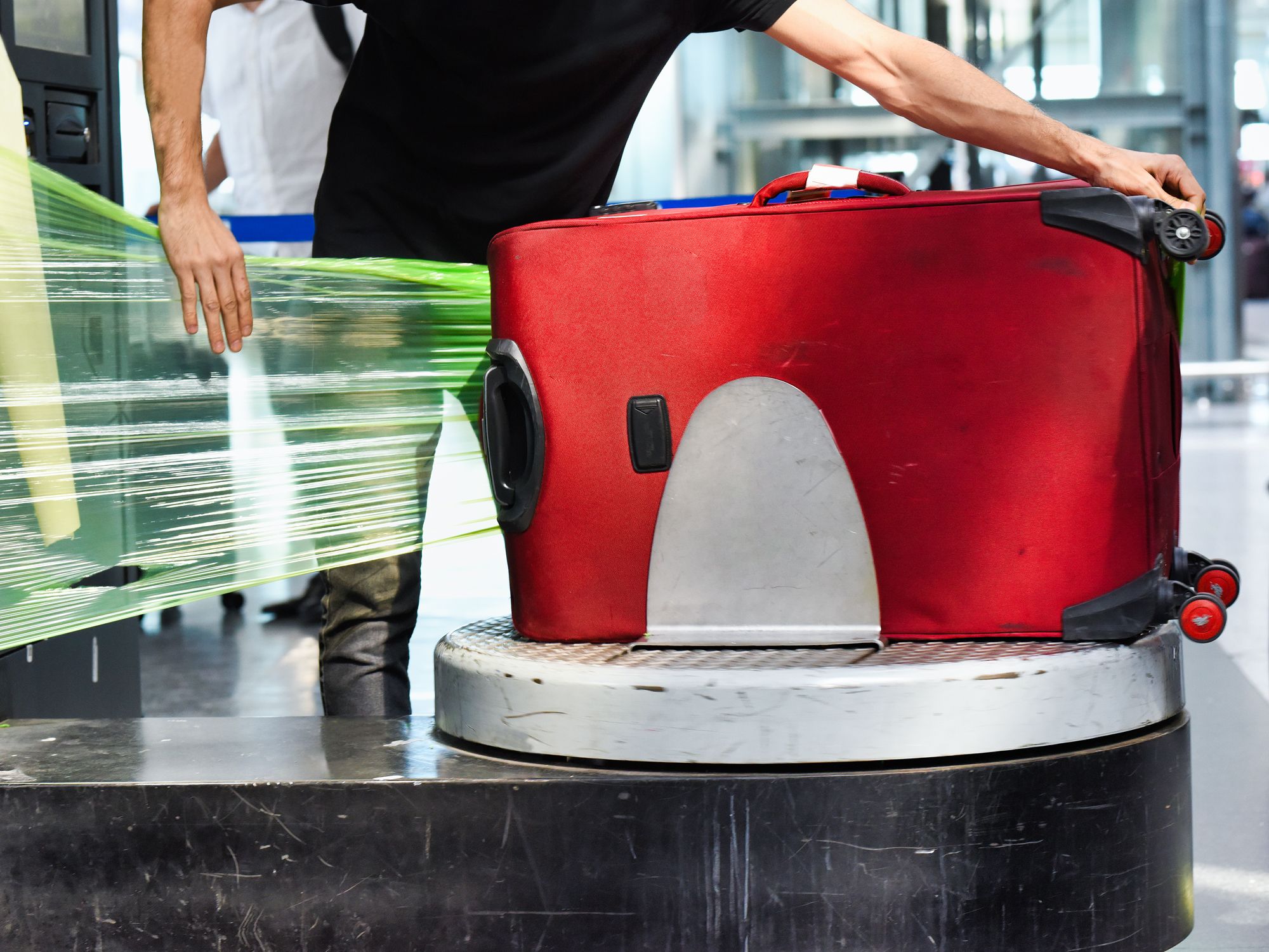 Person shrink-wrapping a red suitcase