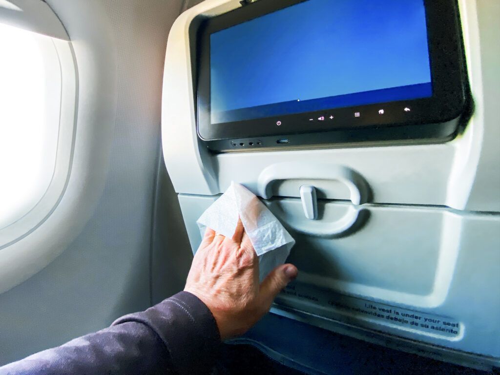 Man wiping down the seat in front of him on an airplane